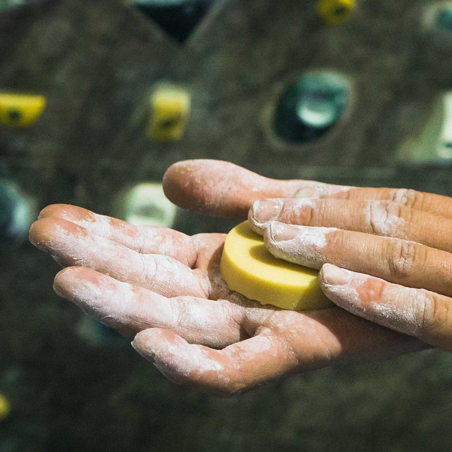 Hand voller Magnesia hält die feste Handcreme vor der Boulderwand