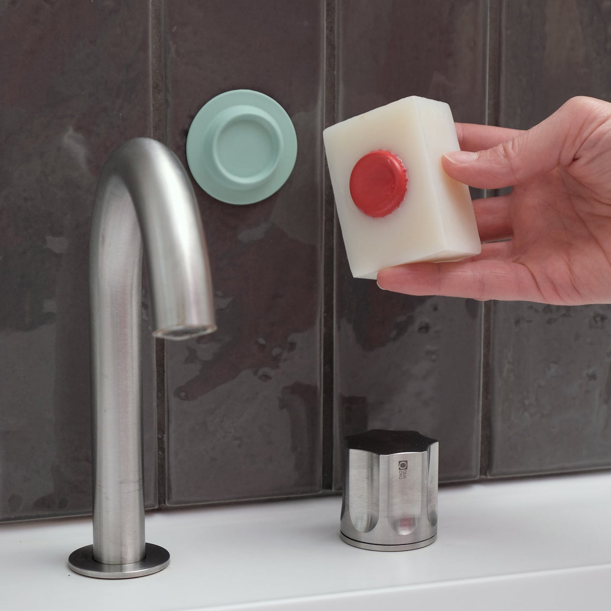 Soap with a pressed-in crown cap next to the mint Soapi magnetic soap holder on a tiled wall